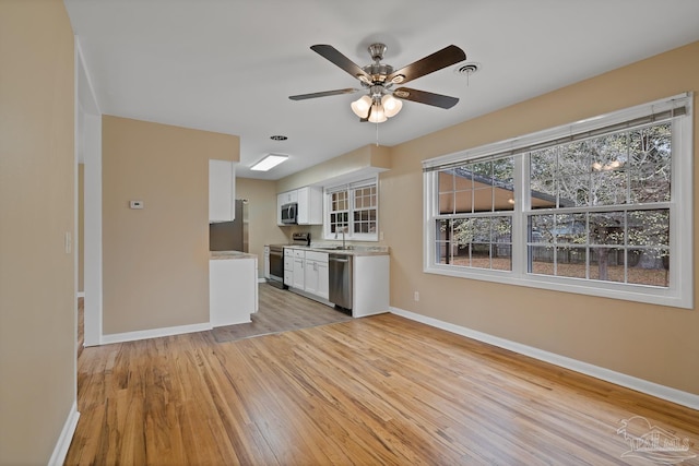 kitchen with a sink, stainless steel appliances, light countertops, white cabinets, and light wood-style floors