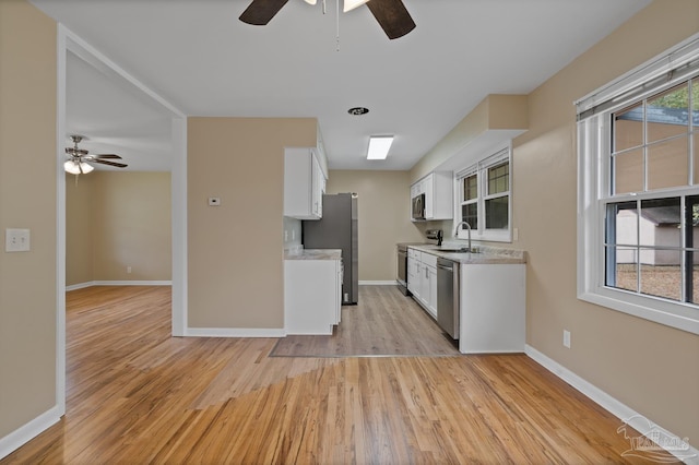 kitchen with light countertops, light wood-style flooring, stainless steel appliances, a ceiling fan, and a sink