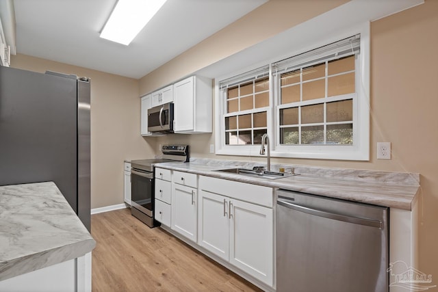 kitchen with light wood-type flooring, light countertops, appliances with stainless steel finishes, white cabinetry, and a sink