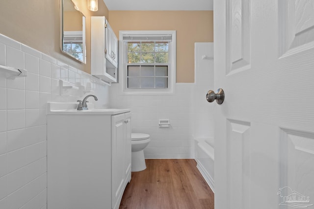 bathroom with toilet, vanity, wainscoting, wood finished floors, and tile walls