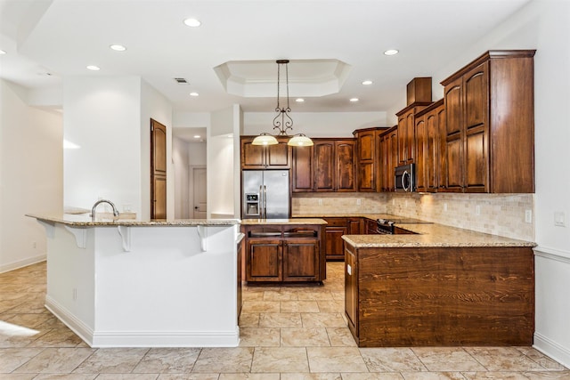 kitchen featuring kitchen peninsula, stainless steel appliances, light stone countertops, and a tray ceiling