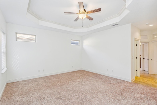 spare room with ceiling fan, a healthy amount of sunlight, light carpet, and a tray ceiling