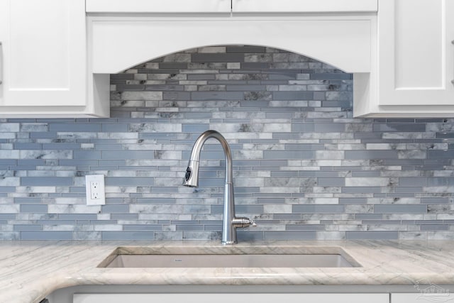 room details featuring white cabinetry, sink, and light stone countertops