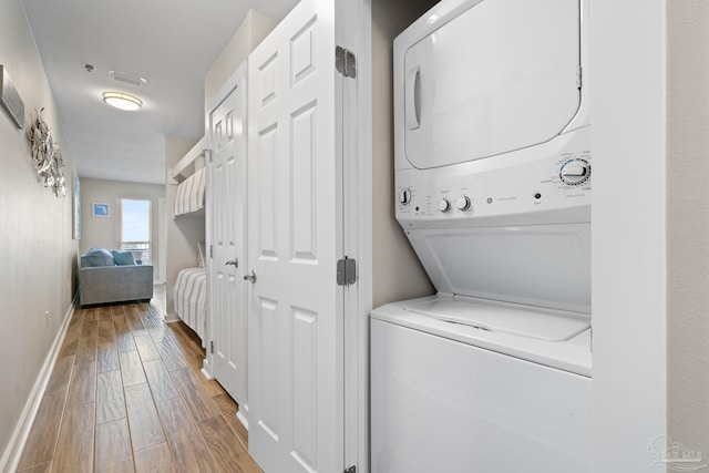 laundry room featuring stacked washer / drying machine and light wood-type flooring