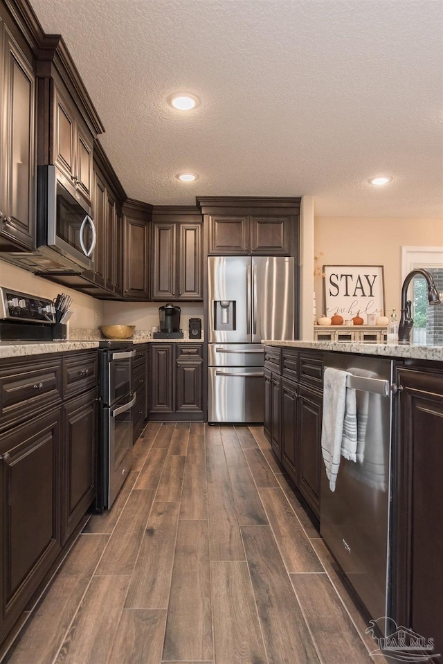 kitchen with dark brown cabinetry, light stone counters, appliances with stainless steel finishes, dark hardwood / wood-style floors, and a textured ceiling