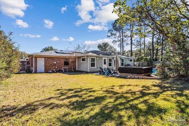 back of house featuring a patio area, a lawn, a hot tub, and solar panels