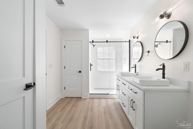 bathroom with visible vents, a walk in shower, wood finished floors, and a sink