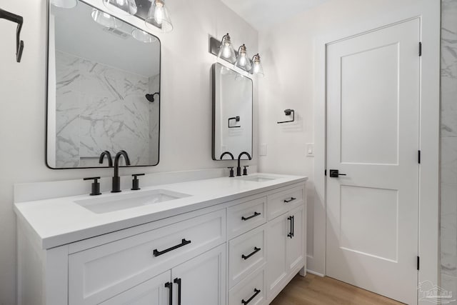 bathroom featuring double vanity, wood finished floors, walk in shower, and a sink