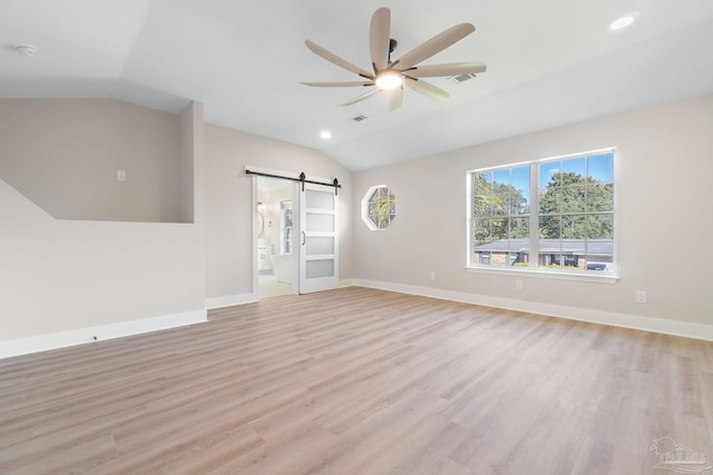 spare room featuring light wood finished floors, baseboards, lofted ceiling, a barn door, and a ceiling fan