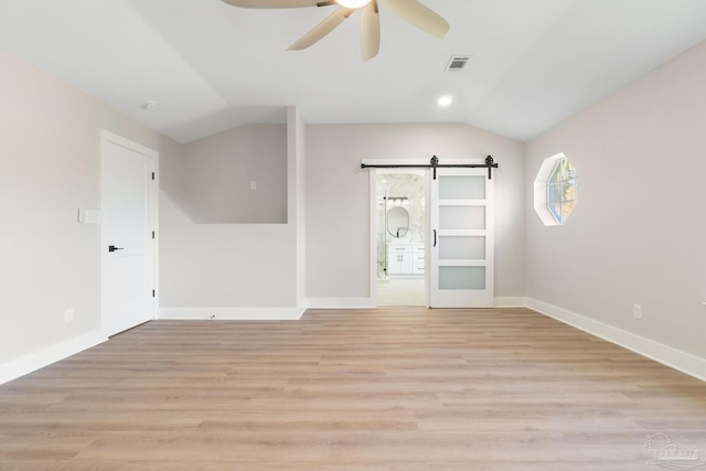 empty room with visible vents, lofted ceiling, ceiling fan, light wood-style floors, and a barn door