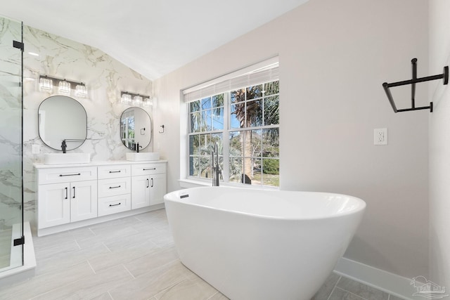 bathroom with a marble finish shower, double vanity, lofted ceiling, a freestanding bath, and a sink