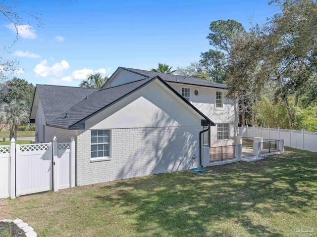 back of house with stucco siding, a fenced backyard, a yard, roof with shingles, and brick siding