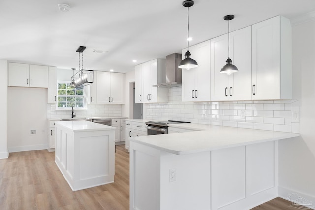 kitchen featuring a sink, light wood-style floors, appliances with stainless steel finishes, wall chimney range hood, and decorative backsplash