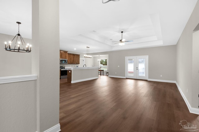 unfurnished living room with a tray ceiling, dark hardwood / wood-style flooring, french doors, and ceiling fan with notable chandelier