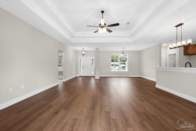 unfurnished living room with a raised ceiling, dark wood-type flooring, ceiling fan with notable chandelier, and sink