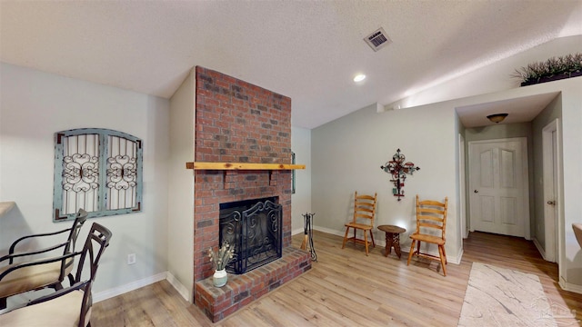 living room featuring a brick fireplace, lofted ceiling, a textured ceiling, and light hardwood / wood-style flooring