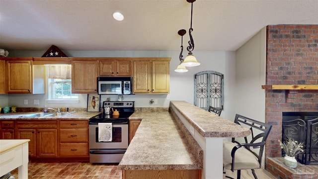 kitchen featuring a sink, light countertops, appliances with stainless steel finishes, a brick fireplace, and decorative light fixtures