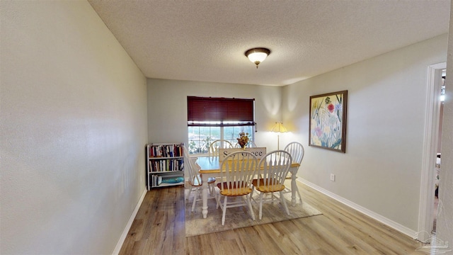 dining space featuring a textured ceiling, baseboards, and wood finished floors