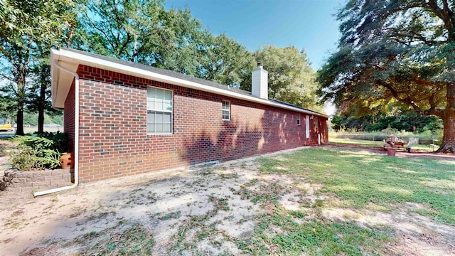 view of side of home with a yard, brick siding, and a chimney