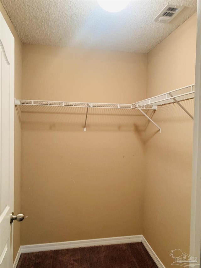 spacious closet with dark carpet and visible vents