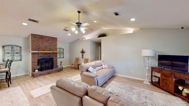 living room with a textured ceiling, vaulted ceiling, ceiling fan, a fireplace, and light hardwood / wood-style floors