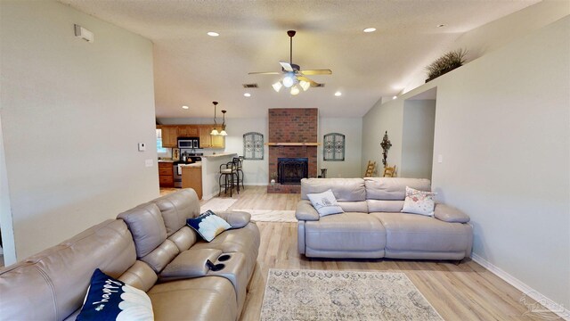 living room with ceiling fan, a brick fireplace, light wood-style flooring, and recessed lighting