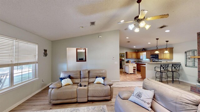 living room featuring a textured ceiling, ceiling fan, light hardwood / wood-style flooring, and lofted ceiling