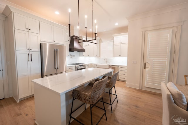 800 N Baylen St, Pensacola, FL 32501 - kitchen with appliances with stainless steel finishes, wall chimney exhaust hood, light wood finished floors, a kitchen bar, and white cabinetry