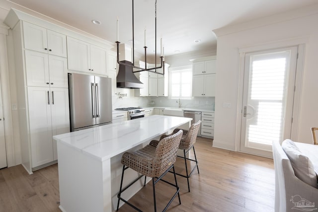 800 N Baylen St, Pensacola, FL 32501 - kitchen with stainless steel appliances, wall chimney range hood, a breakfast bar area, light wood finished floors, and white cabinets