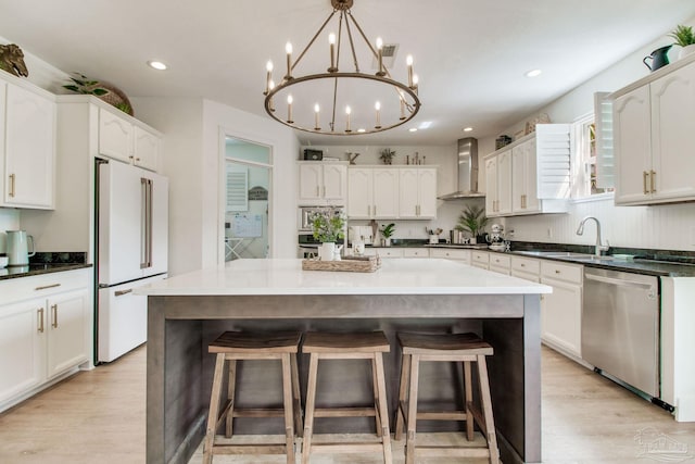 kitchen with a sink, freestanding refrigerator, light wood-style floors, wall chimney range hood, and dishwasher