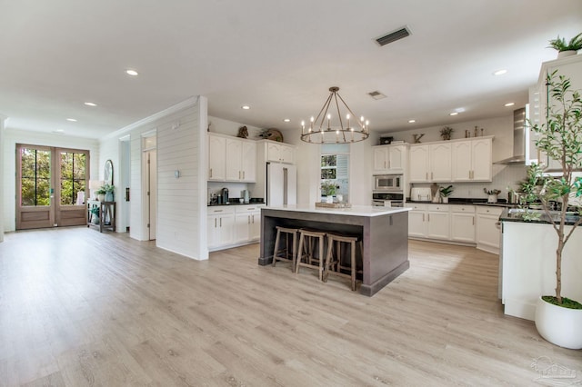 kitchen featuring visible vents, a kitchen island, light wood-type flooring, appliances with stainless steel finishes, and wall chimney exhaust hood