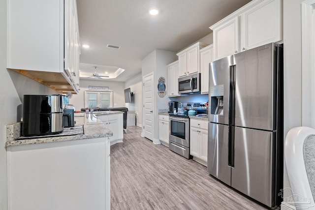 5323 Red Shoulder Rd, Pace, FL 32571 - kitchen with appliances with stainless steel finishes, a tray ceiling, white cabinets, light wood-style flooring, and recessed lighting