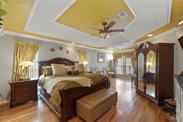 bedroom featuring a raised ceiling, ornamental molding, hardwood / wood-style flooring, and ceiling fan