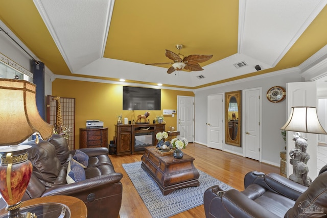 living room with a raised ceiling, ornamental molding, ceiling fan, and light hardwood / wood-style flooring