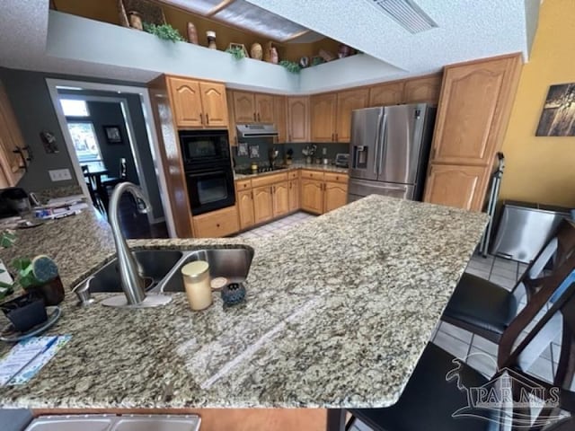 kitchen featuring tile patterned flooring, a textured ceiling, black appliances, a kitchen breakfast bar, and sink