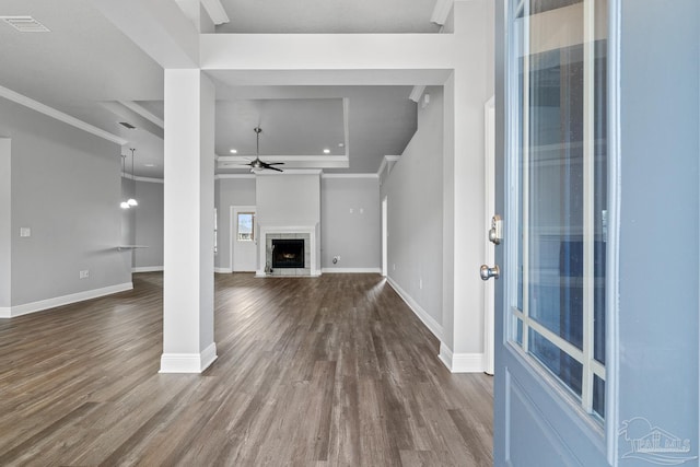 unfurnished living room featuring crown molding, a raised ceiling, hardwood / wood-style flooring, ceiling fan, and a tiled fireplace