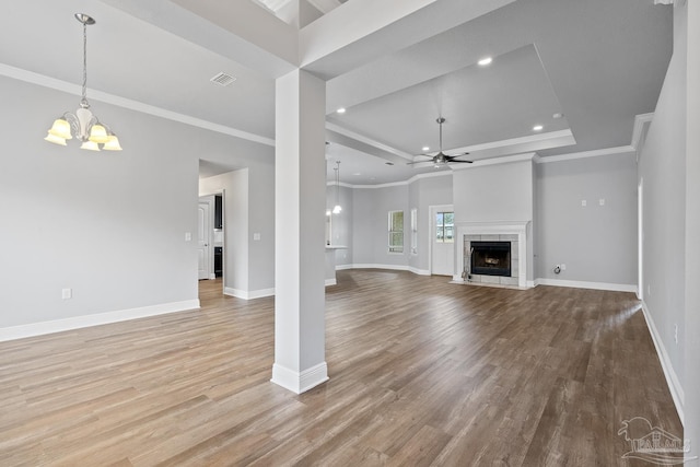 unfurnished living room featuring crown molding, light hardwood / wood-style flooring, a fireplace, ceiling fan with notable chandelier, and a raised ceiling