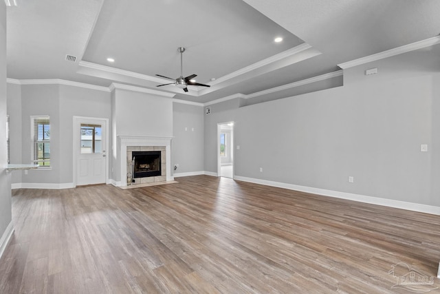 unfurnished living room featuring crown molding, light hardwood / wood-style flooring, a raised ceiling, a tile fireplace, and ceiling fan