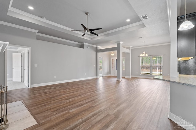 unfurnished living room with ceiling fan with notable chandelier, decorative columns, wood-type flooring, ornamental molding, and a raised ceiling