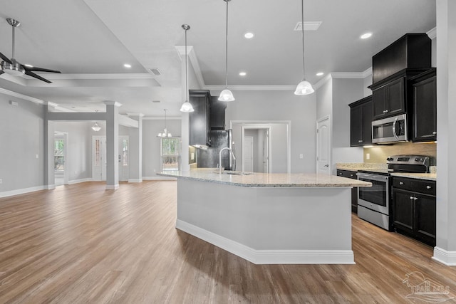 kitchen with sink, decorative light fixtures, light wood-type flooring, appliances with stainless steel finishes, and a kitchen island with sink