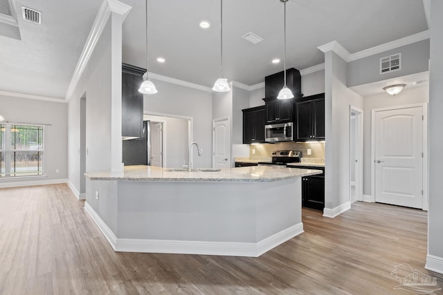 kitchen with appliances with stainless steel finishes, sink, hanging light fixtures, light stone counters, and light hardwood / wood-style floors