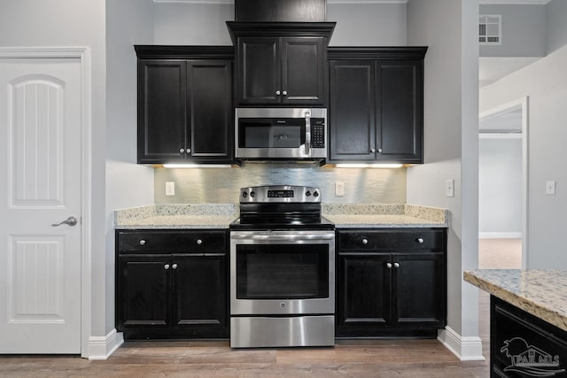 kitchen with hardwood / wood-style floors, backsplash, stainless steel appliances, and light stone countertops