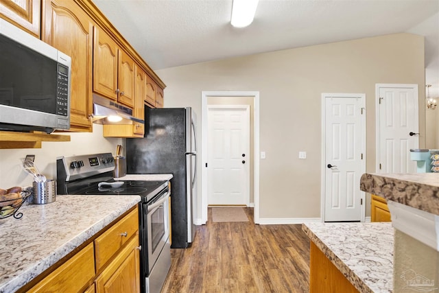 kitchen with appliances with stainless steel finishes, a textured ceiling, vaulted ceiling, dark hardwood / wood-style floors, and light stone counters