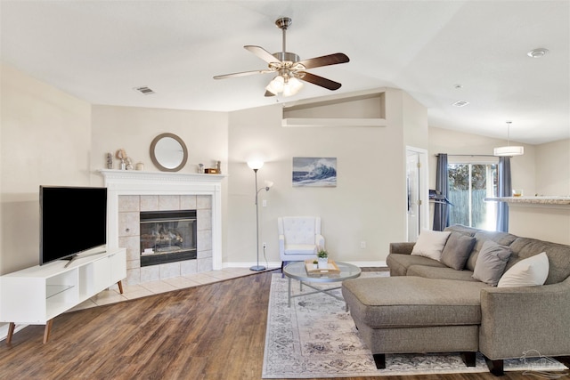 living room featuring ceiling fan, vaulted ceiling, light wood-type flooring, and a tile fireplace