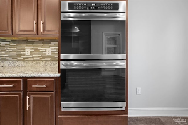 kitchen with dark tile patterned floors, light stone countertops, stainless steel double oven, and decorative backsplash