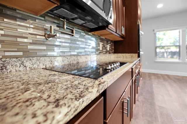 kitchen featuring light hardwood / wood-style flooring, light stone countertops, backsplash, and black electric stovetop