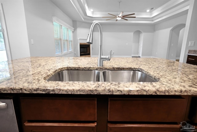 kitchen with light stone countertops, ceiling fan, sink, crown molding, and a tray ceiling