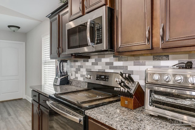 kitchen with light stone counters, stainless steel appliances, light hardwood / wood-style flooring, and backsplash