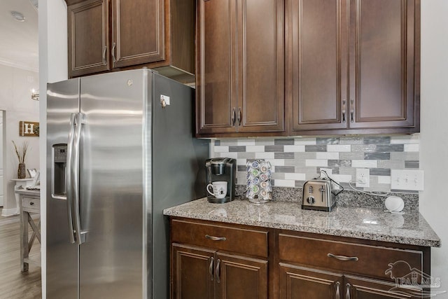 kitchen with stainless steel refrigerator with ice dispenser, light stone countertops, hardwood / wood-style floors, and backsplash