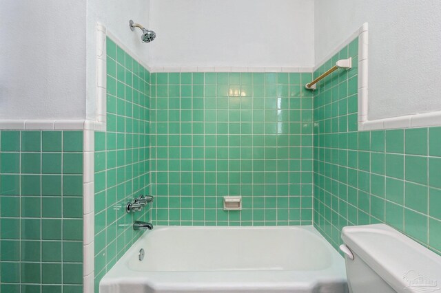 bathroom featuring tiled shower / bath combo, tile walls, and toilet